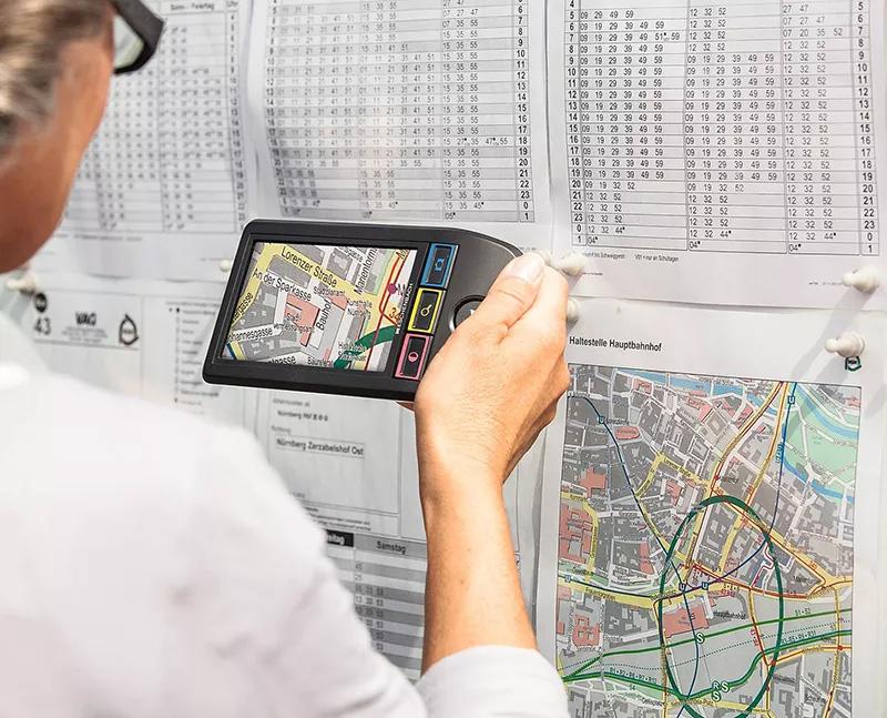 vergroesserndesehhilfe Frau mit elektronischer Sehhilfe vor einem Fahrplan